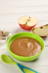 Baby food. Puree of apples in bowl and spoon on white wooden table