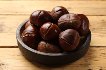 Fresh edible sweet chestnuts in bowl on wooden , closeup