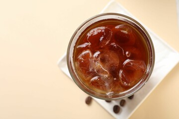 Refreshing iced coffee in glass on beige table, top view. Space for text
