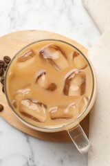 Refreshing iced coffee with milk in glass cup on white marble table, top view