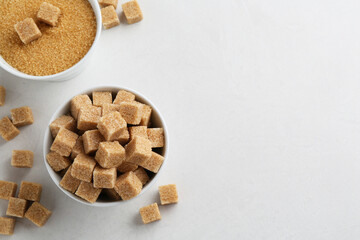 Brown granulated sugar and cubes on white textured table, flat lay. Space for text