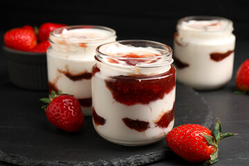 Tasty yoghurt with jam and strawberries on black table, closeup