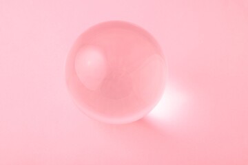 Transparent glass ball on light pink background