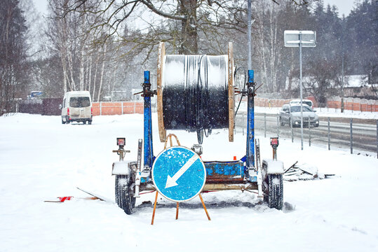 Wooden coil with  fiber optic cable mounted on trailer for easy transportation. Laying optical fiber cable in suburb during snow storm. Cabling, laying of underground communications in winter