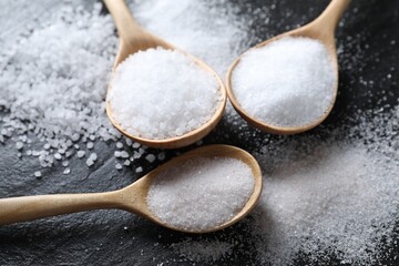 Organic salt in spoons on black table, closeup