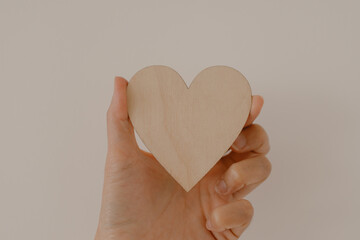 Woman hand holding wooden heart showing empty space, isolated over white background wall.