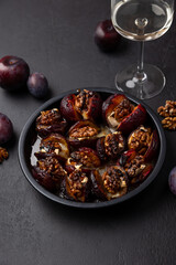 Plums baked with Camembert cheese, walnuts, honey and glass of white wine. Popular hot appetizer on a black plate. Selective focus, close-up.