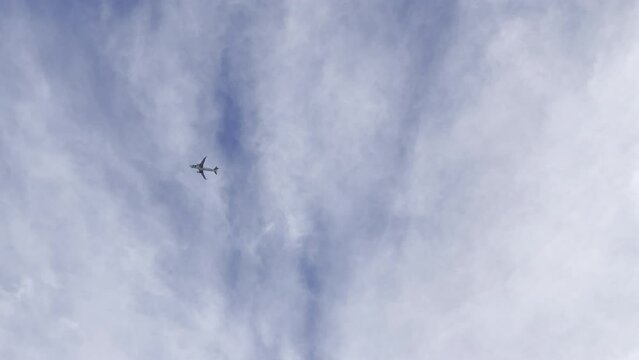 Aeroplane above passing by and flying through clouds overhead in Lisbon, Portugal, Europe, with airplane flying through blue sky, sunny, bright, plane spotting