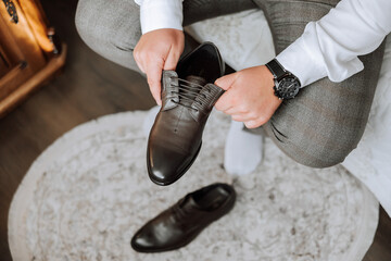 A man is putting on his shoes while sitting on a sofa in a hotel room. A young entrepreneur is preparing to go on a business trip. Businessman preparing for travel in home bedroom early in the morning