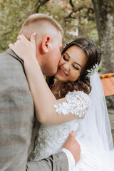 A young bride and groom tenderly embrace in the rays of the autumn sun. Tender and beautiful young girl bride. A man kisses his beloved. Against the background of a beautiful garden