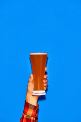 Man holding long glass with fresh beer isolated on blue background. Traditional taste. Party....