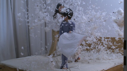 Children engaged in pillow fight with feathers flying everywhere in the air captured in super slow...