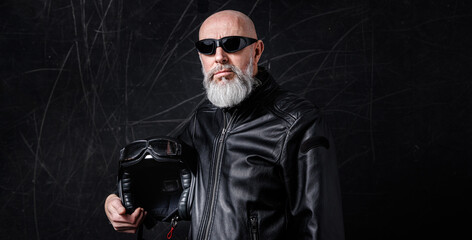 Portrait d'un motard biker homme avec un casque noir et une veste en cuir et des lunettes de protection et une barbe grise vintage