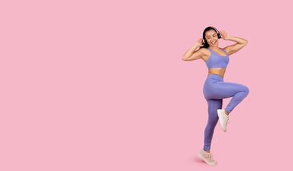 Joyful woman dancing in sportswear with headphones on pink backdrop