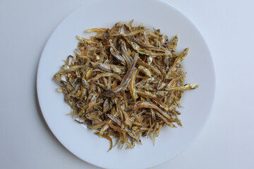 Dried anchovy fish, uncooked, on a white plated, white background. Preserved with salt. Flat lay or top view