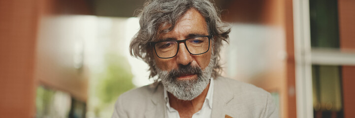 Clouse up, mature businessman with beard in eyeglasses wearing gray jacket sits on cafe, Panorama....