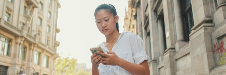 Young woman uses mobile phone while standing next to the road. Girl is waiting for taxi, Panorama