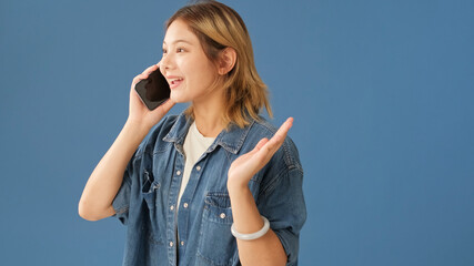 Surprised young woman dressed in denim shirt speaks on mobile phone receiving good news, winning...