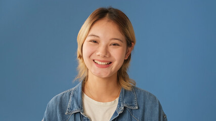 Smiling woman looks at camera isolated on blue background in studio