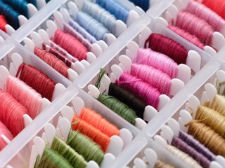 Bobbins with different colour embroidery threads in a plastic sorting box.
