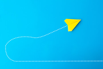 Top view of yellow paper airplane making a U turn on blue background