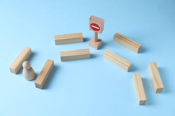 Overcoming barries for development and success. Wooden human figure movement blocked by road Stop sign on light blue background