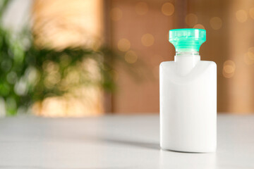 Mini bottle of cosmetic product on white table against blurred background. Space for text
