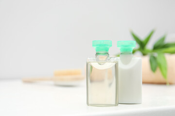 Mini bottles of cosmetic products on white table against blurred background. Space for text