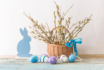 Happy easter holidays concept: Easter eggs, rabbit and bouquet of willow in wicker basket on a white background
