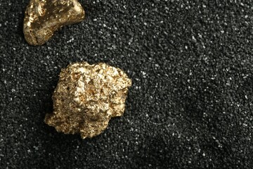 Shiny gold nuggets on black sand, above view. Space for text