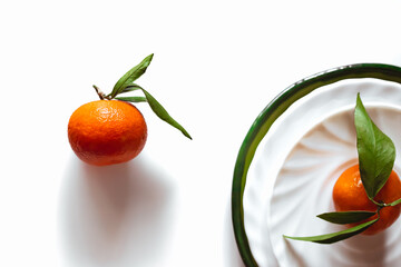 Mandarin or orange on white plate. Citrus clementine with green leaves. Ready to eat tangerine on...