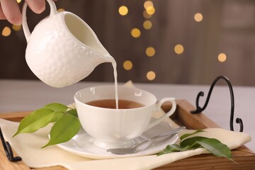 Woman pouring milk into cup with aromatic tea at table, closeup