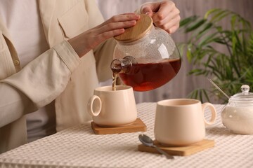 Woman pouring aromatic tea into cup at table, closeup