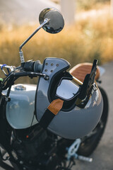 A motorcyclist's helmet with goggles hangs on the handle of a cafe racer.
