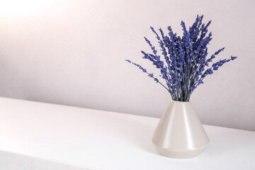 Bouquet of beautiful preserved lavender flowers on white wooden table near beige wall, closeup. Space for text