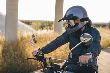 A man with a vintage motorcycle on the highway at sunset. A man drives a cafe racer. Biker...