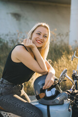Fototapeta na wymiar Biker girl sits on a motorcycle. Young beautiful blonde woman sitting on a motorcycle on the highway at sunset.