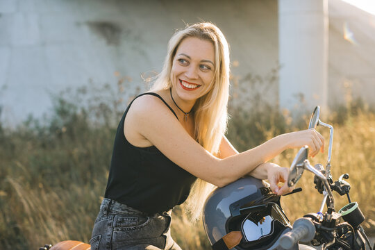 Biker girl sits on a motorcycle. Young beautiful blonde woman sitting on a motorcycle on the highway at sunset.