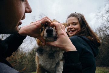 A woman holds a dog in her arms, and a man on the other hand made a heart out of his fingers and...