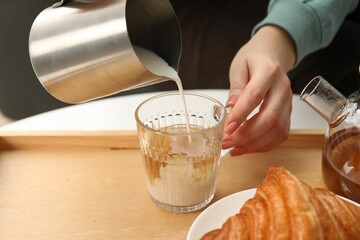 Woman pouring milk into cup with aromatic tea at table indoors, closeup