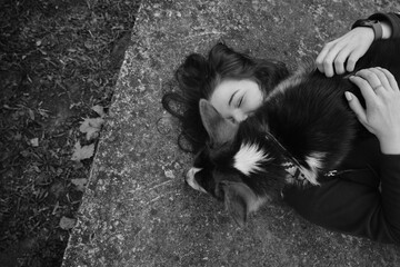 Young woman lies on a concrete slab in the park and hugs her dog. Welsh corgi pembroke and female...