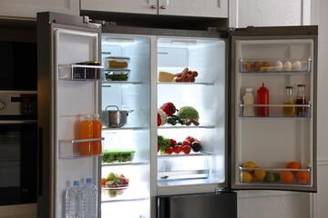 Open refrigerator full of different products in kitchen