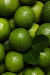 Fresh ripe limes and leaves with water drops as background, top view