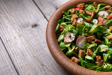Lamb's lettuce salad with radish, nigella seeds, and roasted sunflower seeds in a ceramic plate. Rustic wooden table. Copy space.