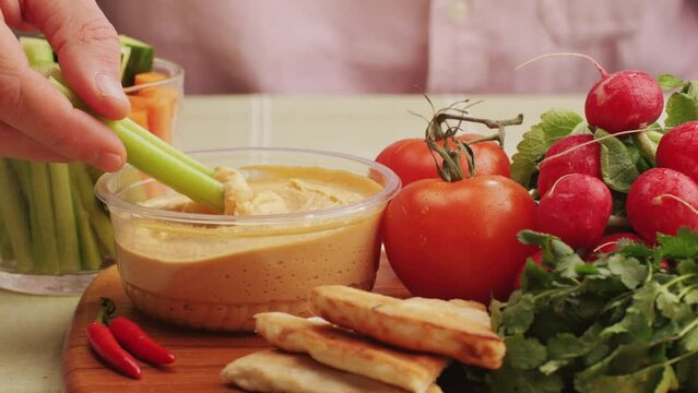 Hummus among fresh vegetables on table close-up. Dipping vegetable slice in hummus. Hummus or fava, a healthy snack of legumes and chickpeas. Kosher healthy vegan food. Lean, vegetarian dish
