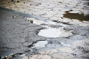 Potholes in the road, a dilapidated asphalt road with rainwater in the middle.