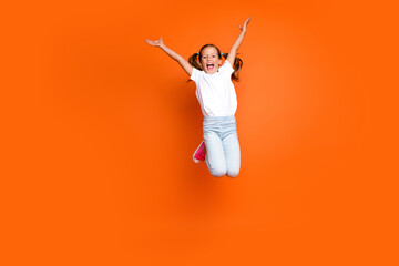 Full size photo of cheerful little girl raise arms jumping have good mood isolated on orange color background