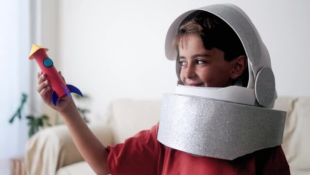 Astronaut child playing with rocket toy. Kid dreams of travel in space with crafty helmet