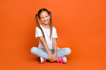 Full size photo of adorable positive schoolkid sit floor empty space ad blank isolated on orange color background
