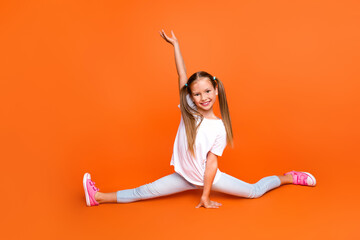 Full size photo of positive sportive flexible schoolkid split legs raise hand isolated on orange color background